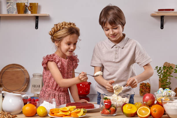 los pequeños amigos están haciendo un pastel juntos en una cocina contra una pared blanca con estantes. - beauty beautiful braids dairy product fotografías e imágenes de stock