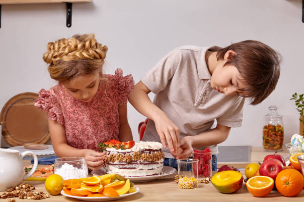 los pequeños amigos están haciendo un pastel juntos en una cocina contra una pared blanca con estantes. - beauty beautiful braids dairy product fotografías e imágenes de stock