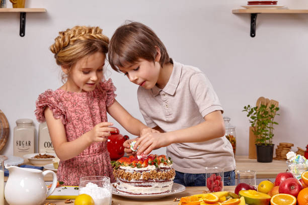 los pequeños amigos están haciendo un pastel juntos en una cocina contra una pared blanca con estantes. - beauty beautiful braids dairy product fotografías e imágenes de stock