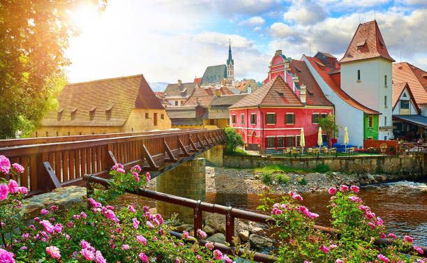 Cesky Krumlov, Czech Republic. Wooden bridge on Vltava river Czech Krumlov, (Cesky Krumlov), Czech Republic. Wooden bridge over river Vltava. Vintage picturesque old town with colorful houses and chapel of church. Rose flowers on bank. Sunny summer day. czech republic stock pictures, royalty-free photos & images