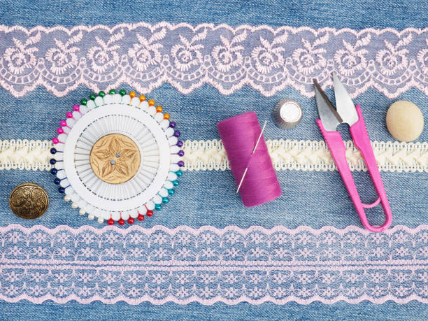istock Pink and beige lace, scissors, buttons, pins, threads with needle, thimble on a jeans background. Sewing still life 1157967195