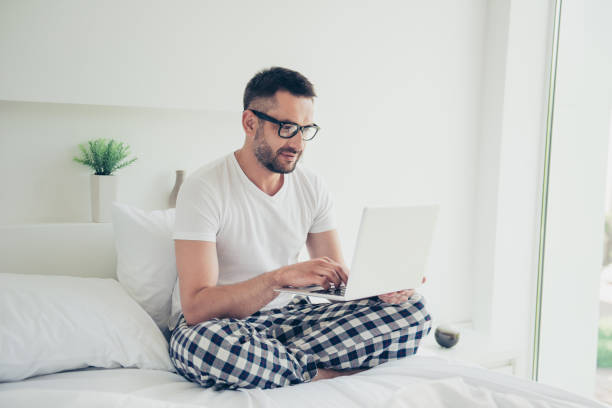 istock Close up photo amazing he him his guy weekend workaholic notebook writing check currency speak skype partners white nightwear sleep wear t-shirt checkered pants sitting bed bright room house indoors 1157968130