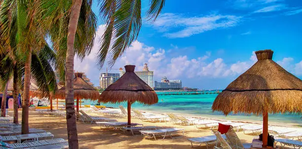 Panoramic view of the tropical beach in Cancun, Mexico, with straw beach umbrellas and turquoise sea in the background.