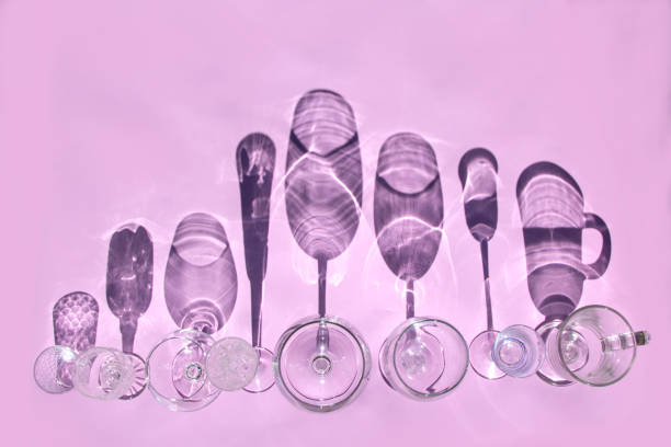 Empty glasses of different forms for wine, whiskey, mulled wine, vodka, liquor stand in row on pink background in sunlight with shadows. Top view, flat lay.