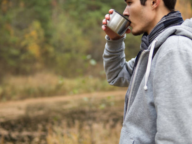 istock man drinking hot tea from a thermos during a walk through the autumn forest. close-up with copy space 1157970761