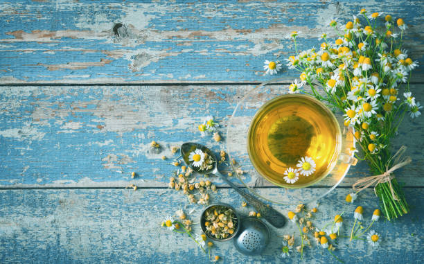 чашка травяного чая с ц�ветами ромашки на выдержавной голубой деревянной доске - chamomile plant стоковые фото и изображения