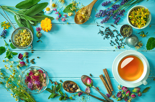 Cup of healthy herbal tea with mint, sage, cinnamon, dried rose, chamomile and lavender flowers on blue wooden table. Top view