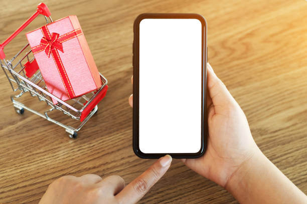 istock female hands holding mobile smartphone with empty screen and gift box background. 1157972110