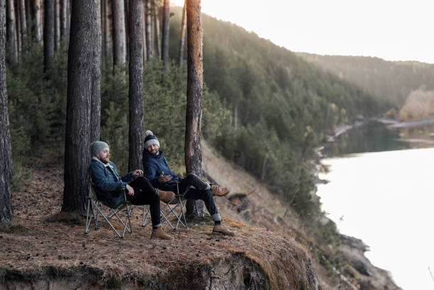 istock Men sitting in folding chairs on cliff by river 1157972527