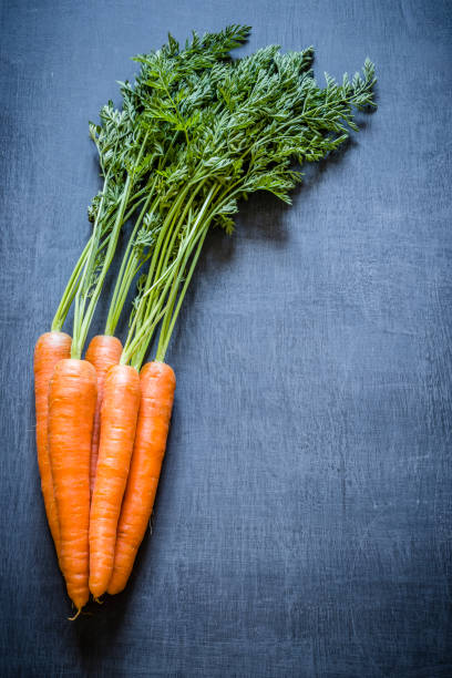 Fresh carrot bunch with copy space on dark gray textured background, Carrots has it stem and are at the left side of the image leaving a useful copy space at the right side. Low key DSLR photo taken with Canon EOS 6D Mark II and Canon EF 24-105 mm f/4L