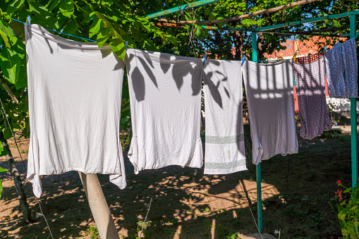 Laundry hanging out to dry outdoors in summer under sun, under tree partly shadow