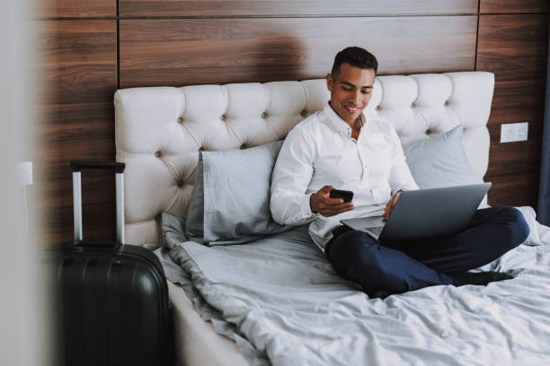 l'homme gai utilise des technologies modernes dans la chambre d'hôtel - hotel wireless technology bedroom hotel room photos et images de collection