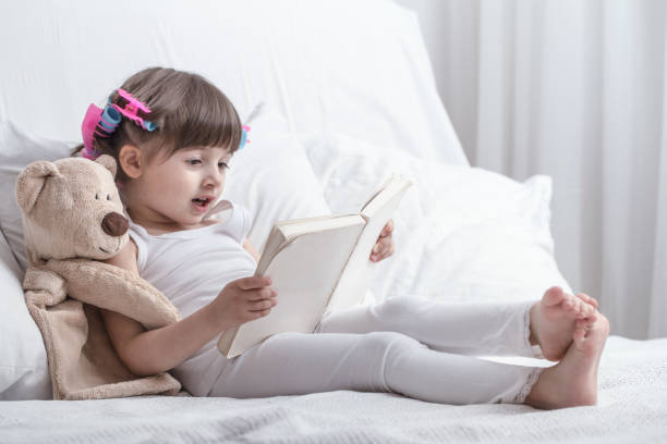 istock Cute little girl smiling while lying in a cozy white bed 1157980126