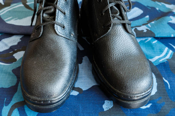 une paire de bottes noires d'armée sur le tissu avec le camouflage bleu. pas de gens. bottes d'armée pour le soldat. la partie avant de la chaussure. - combat boots photos et images de collection