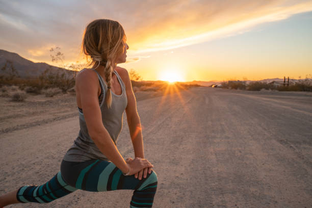 Young woman stretching body after jogging, sunset at the end of the road; female stretches body in nature stock photo
