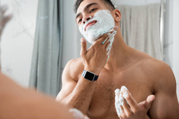 young man gently spreading shaving foam on face - shaving men shaving cream mirror imagens e fotografias de stock