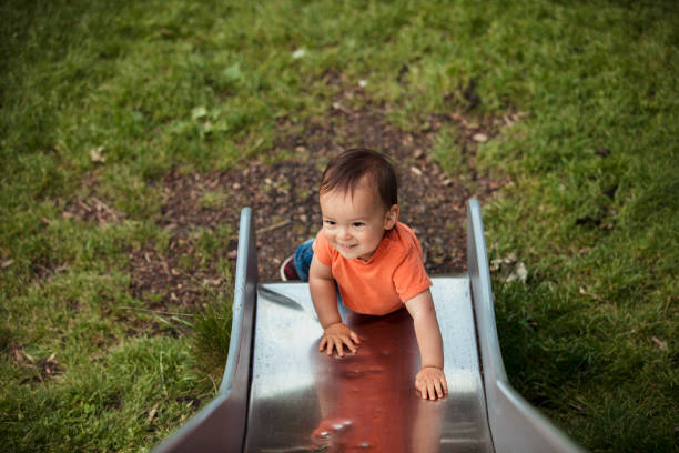 An adorable baby boy is climbing up a slide in the park looking happy and full of vitality.