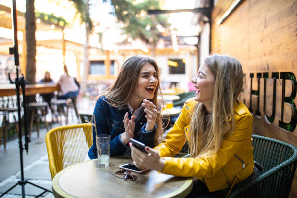 istock Girls having fun while using phone and drinking coffee in sidewalk cafe 1157992151