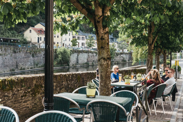 People sitting at cafe tables by the river Our in Vianden, Luxembourg. Vianden, Luxembourg - May 18, 2019: People sitting at cafe tables by the river Our in Vianden, a town in Luxembourgs Ardennes region known for the centuries-old hilltop Vianden Castle. vianden stock pictures, royalty-free photos & images