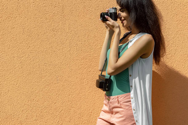 istock Charming young lady with retro camera standing against light orange wall 1157995599