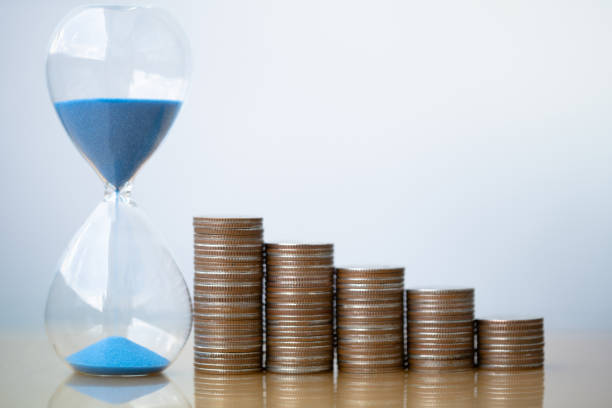 istock Hourglass blue sand and stack of coins. 1157995741