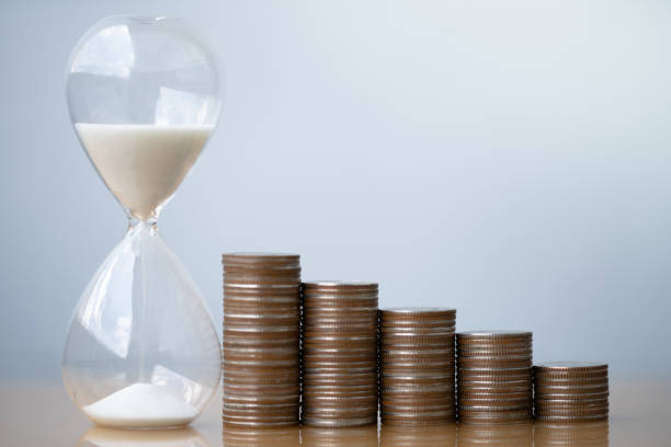 istock Hourglass blue sand and stack of coins. 1157995742