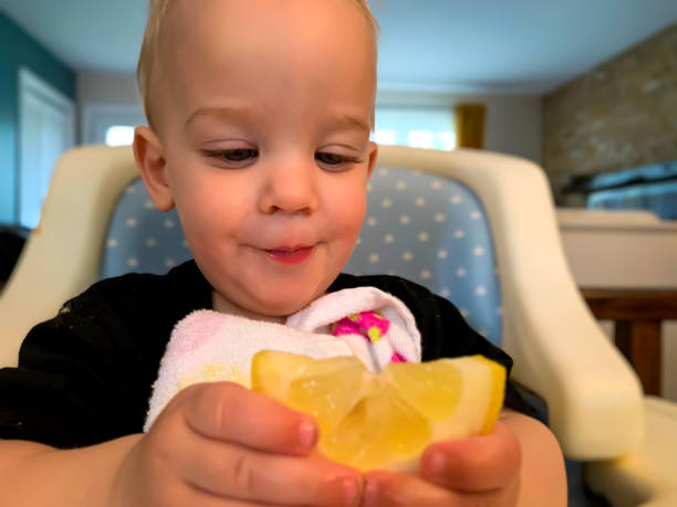 baby jongen eten citroen met zijn handen. - foto’s van jongen stockfoto's en -beelden