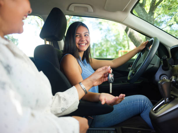 Teenage girl driving for the first time A side view photo of a teenage girl in a car as her mother sits next to her and hands her the keys to drive. medium shot stock pictures, royalty-free photos & images