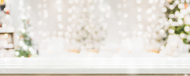 Empty white wold table top with abstract warm living room decor with christmas tree string light blur background with snow,Holiday backdrop,Mock up banner for display of advertise product