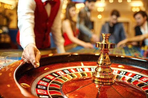 Three people at the roulette table betting with casion coins.