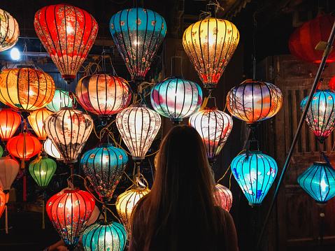 A rear-view shot of an unrecognisable woman standing in a market stall looking at the homemade lanterns on display.