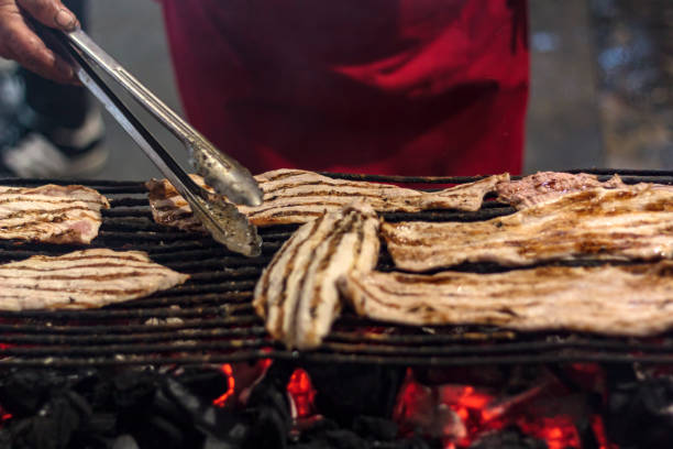 woman grilling slices of pork steaks "febras" on the street during the feasts of the popular saints - santos populares imagens e fotografias de stock