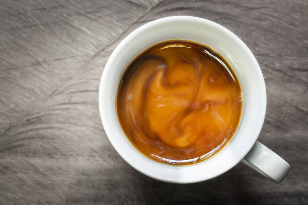 tazza di caffè con latte che scorre su sfondo di legno, colpo in testa. - tipping over foto e immagini stock