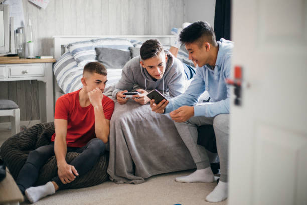 Teens Using Social Media Three teenage boys relaxing and having fun while playing on a games console in a bedroom. adolescence stock pictures, royalty-free photos & images