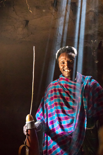 Maasai man inside a traditional house holding a calabash, traditional dish to store milk