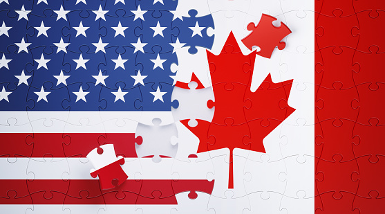 Jigsaw puzzle pieces textured with American and Canadian flags. Horizontal composition with copy space and selective focus. Solution concept.