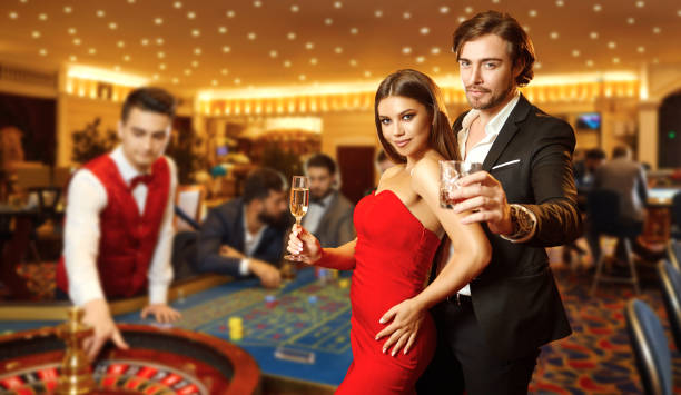 Beautiful glamour couple against the background of casino poker roulette. Beautiful glamour couple with glasses of alcohol in hand are standing against the background of casino poker roulette. couple at the casino stock pictures, royalty-free photos & images