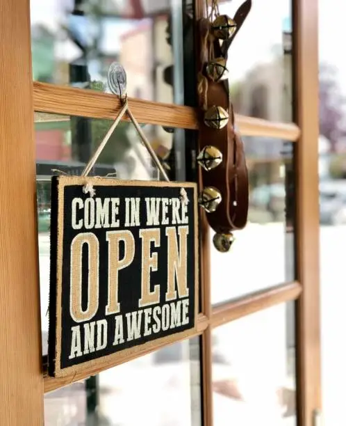 Open sign hanging on the open door of a small retail business. Bells hang from the door to let the shop owner they have a customer