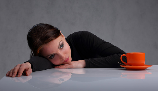 Portrait of a lonely, bored woman with an orange Cup of coffee