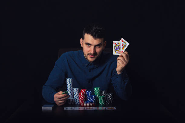 zuversichtlicher pokerspieler sitzt am casino-tisch und zeigt seine gewinnkarten über schwarzem hintergrund. erfolgskonzept für glücksspielturniersieger. chips und würfel - table house of cards strategy business stock-fotos und bilder