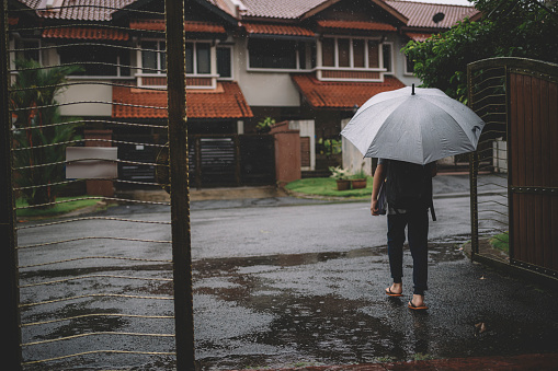 an asian chinese boy going to school during raining day carrying an umbrella in front of the house