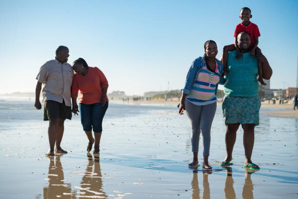 Multi-generational family enjoying at beach Full length of multi-generational family enjoying at beach. Males and females walking on shore against clear blue sky. They are wearing casuals. family beach vacations travel stock pictures, royalty-free photos & images