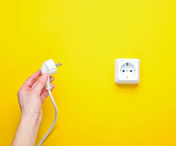 istock Female hands plug in power plug into electro outlet on yellow background. Minimalism. Top view 1158026897
