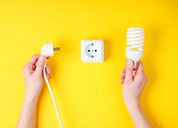istock Female hands plug the power plug into electrical outlet while holding spiral light bulb on yellow background. Minimalism. Top view 1158026942