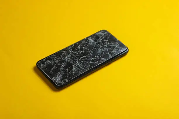 Photo of Smartphone with broken protective glass on yellow background.