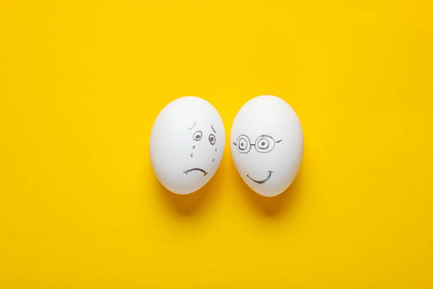istock Sad and happy face eggs on yellow background. Top view 1158028366