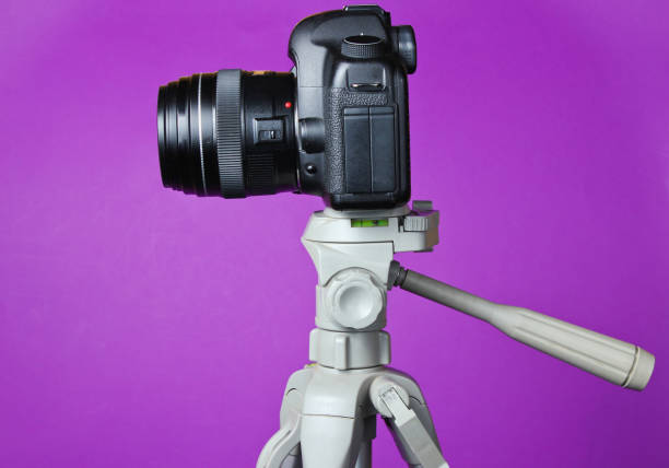 istock Modern digital camera with a tripod on purple background. Front view 1158028668
