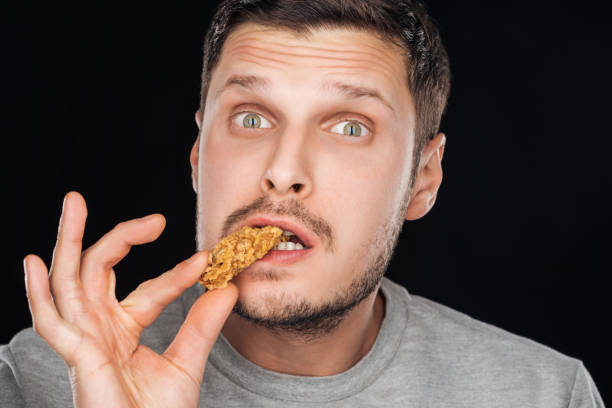 istock handsome man eating chicken nugget while looking at camera isolated on black 1158030500