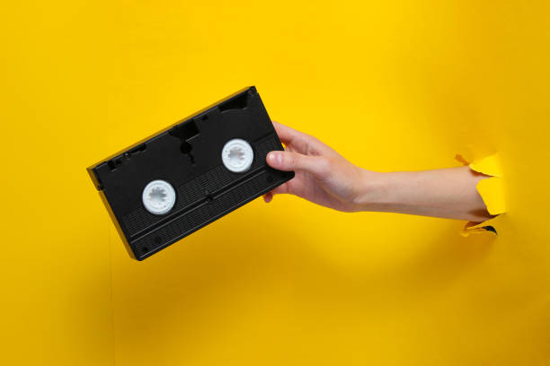 la main femelle retient la cassette vidéo par le fond déchiré de papier jaune. concept rétro minimaliste - playback photos et images de collection