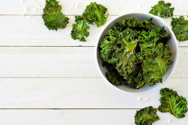 Healthy kale chips, above view corner border on white wood